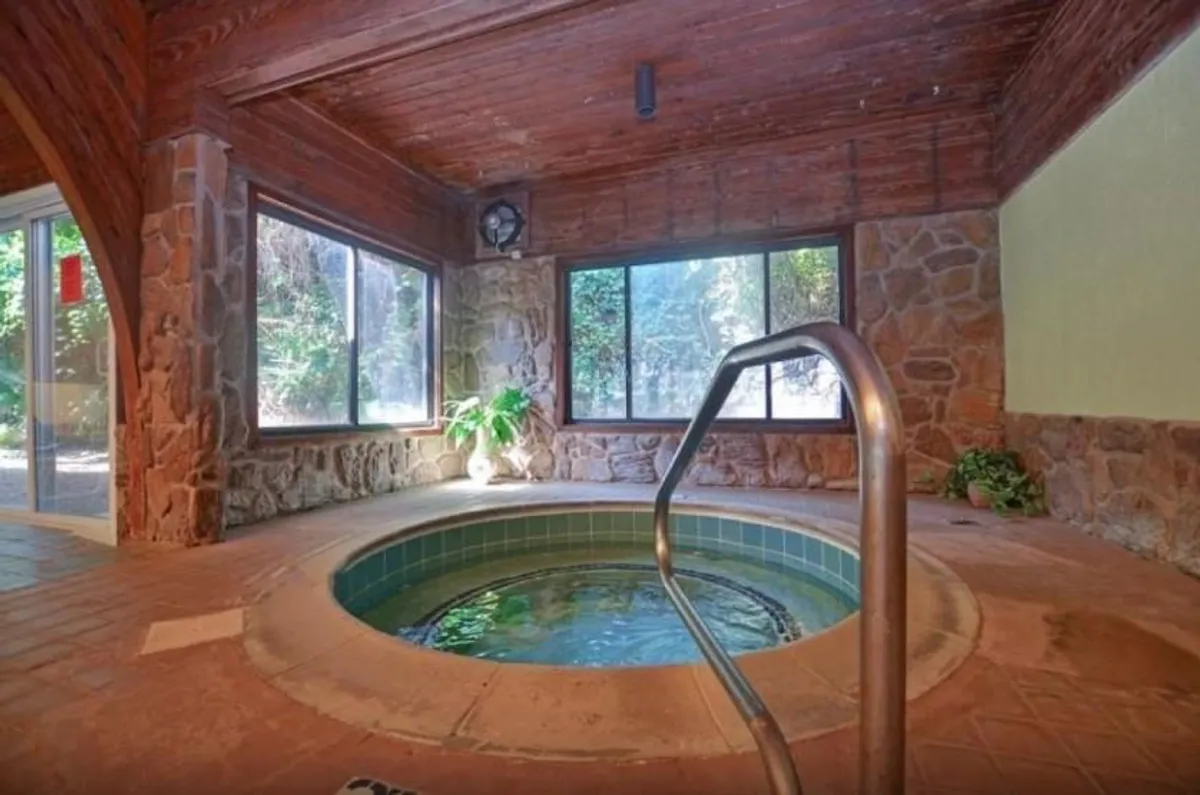 This interior scene showcases a tranquil hot tub surrounded by natural stone walls, large windows filling the space with light, and lush indoor plants. The space radiates calm and rejuvenation, inviting guests to unwind after a busy day of activities.