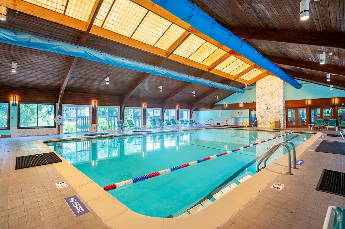 A bright, welcoming indoor pool area, featuring a wooden ceiling, large windows with abundant natural light, and a spacious swimming area ideal for year-round recreation. The setting invites relaxation and friendly community interactions.