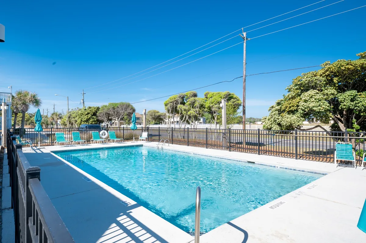 A vibrant outdoor swimming pool area featuring inviting blue water, lounge chairs, umbrellas, and secure fencing. The scene hints at relaxation and fun, with serene poolside vibes and ample space for sunbathing or socializing.
