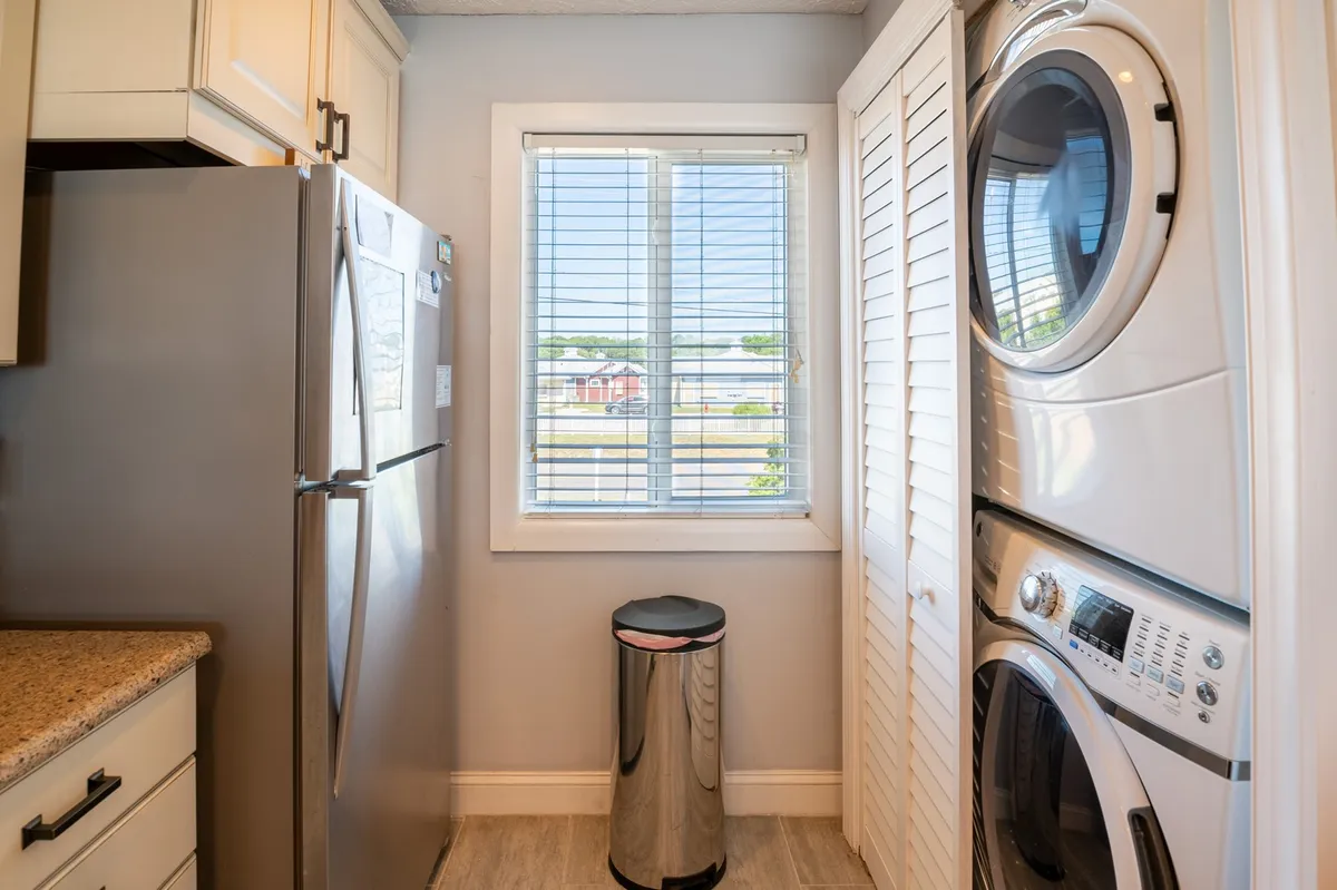 A practical laundry area featuring a washing machine and dryer set beneath a sunny window, with a refrigerator nearby. The setup exudes everyday convenience for longer stays at the retreat.