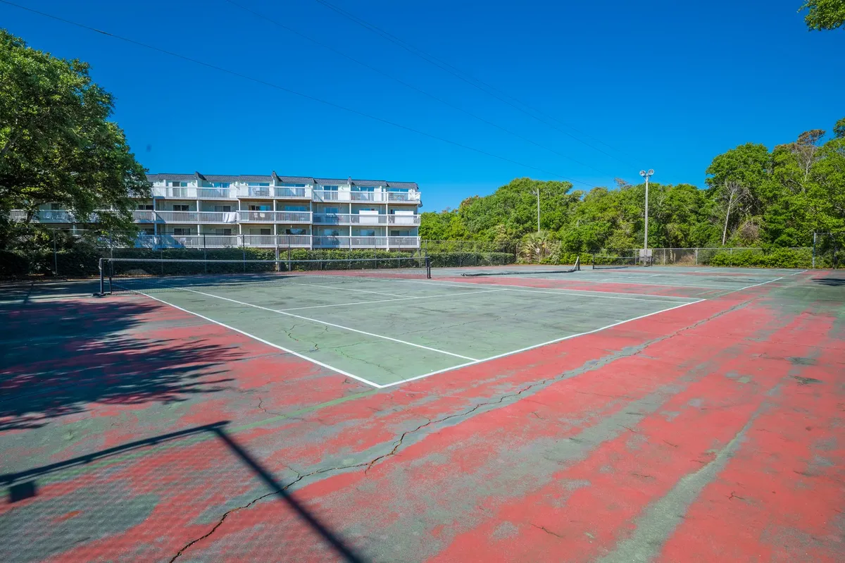 An exterior view of the well-maintained tennis court framed by lush greenery and the adjacent apartment building. The court is ready for friendly matches and energetic games, with crisp lines and nets in place, offering a lively space for exercise and competition.